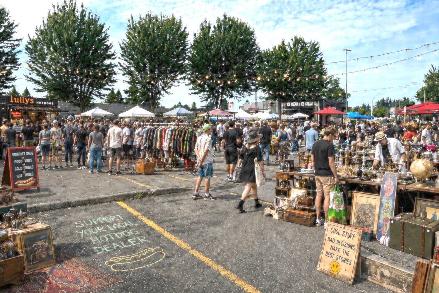 A crowded outdoor flea market beside the Lully’s hot dog stand, with string lights and vendor tables.